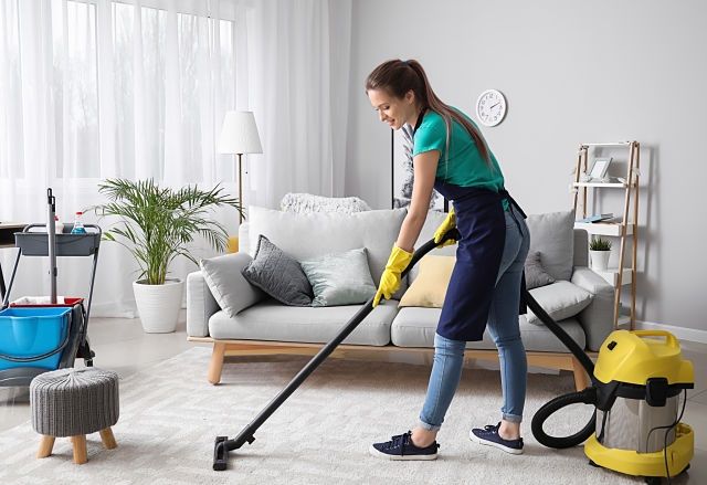 Female janitor with vacuum cleaner in room